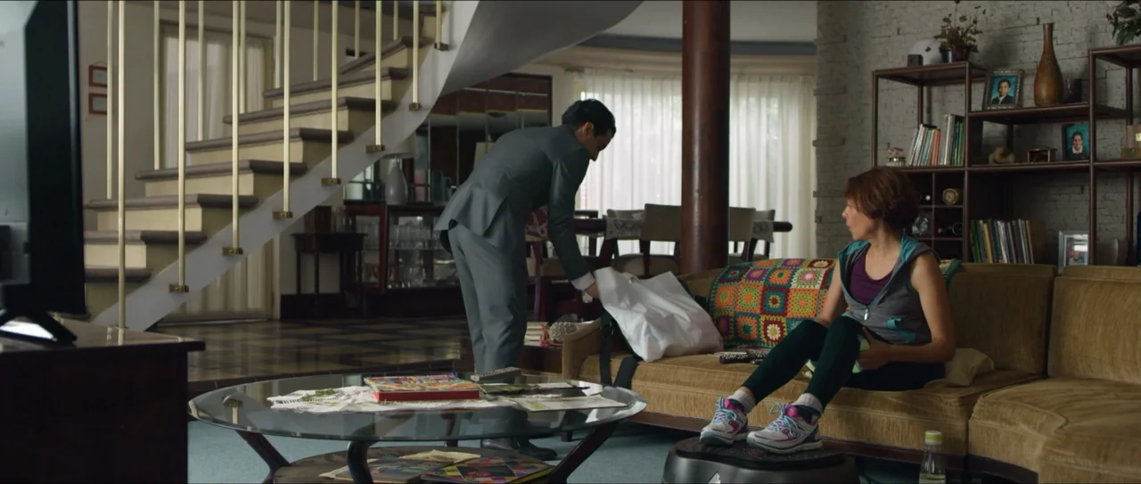 Mirreyes vs Godínez (2019) movie still: wide — A multi-level living room features a wooden staircase, glass coffee table, and a crochet-covered…