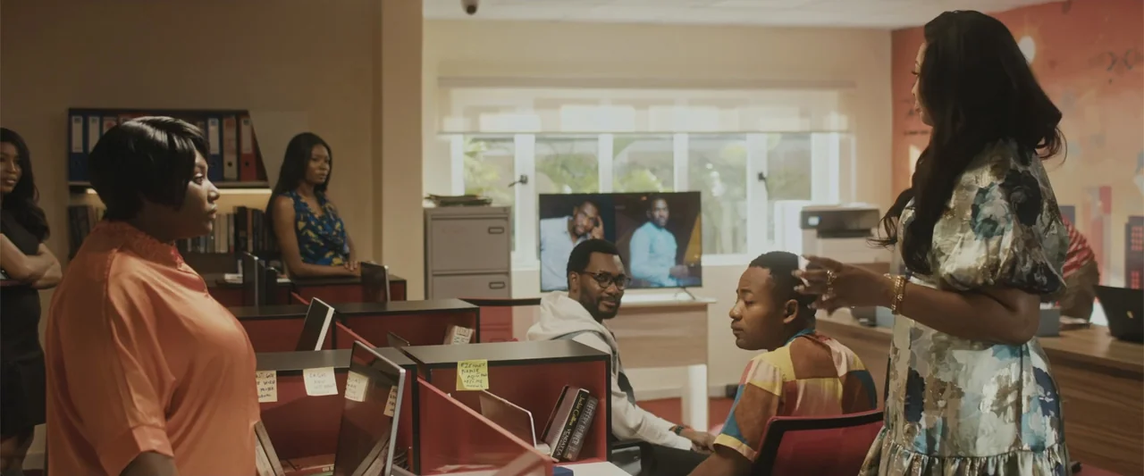 Casa De Novia (2024) movie still: medium — A modern open-plan office features cubicle dividers, a flat-screen display, and shelving units. A small…