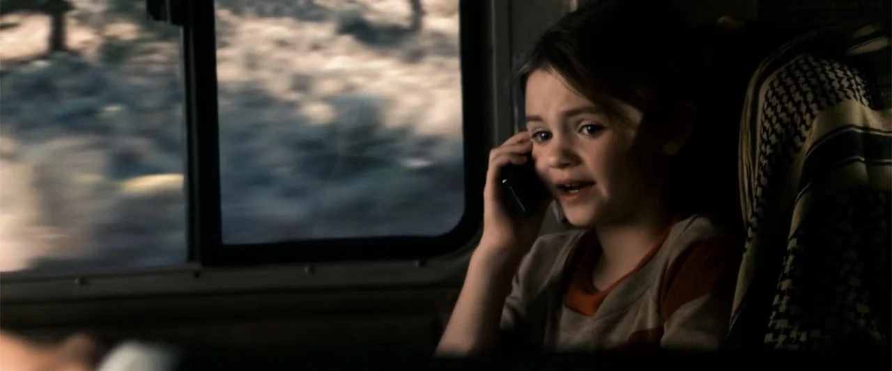 2012 (2009) movie still: medium — A view from inside a moving vehicle with blurred trees visible through the window. A young girl sits in a seat…