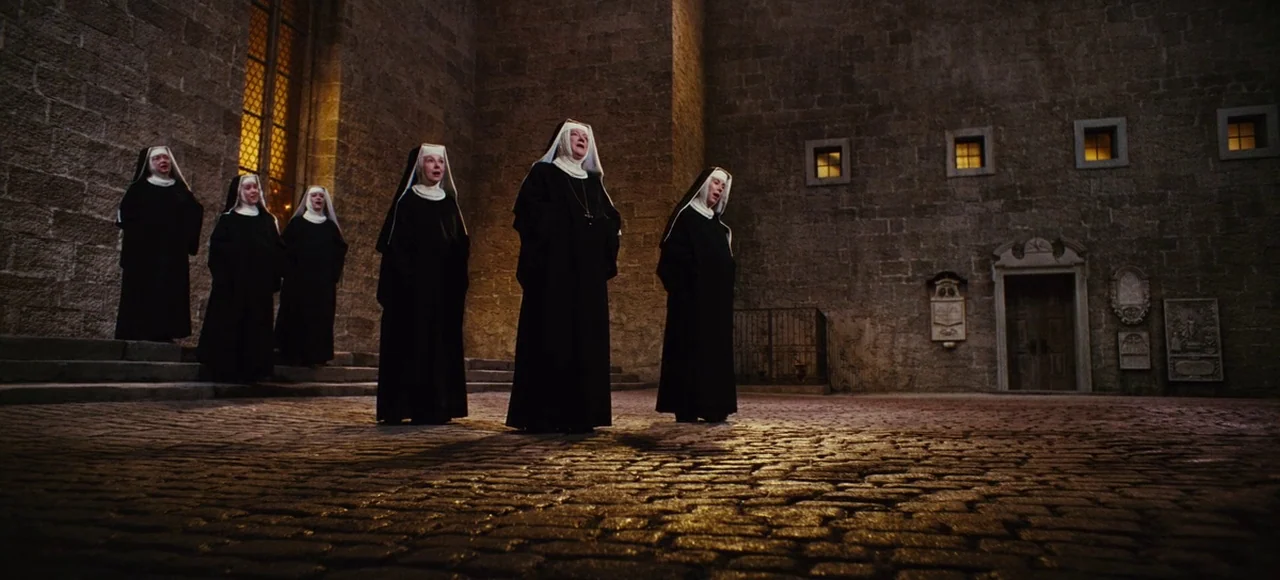 The Sound of Music (1965) movie still: wide — A stone courtyard with high grey masonry walls features several small square windows at night. A group…