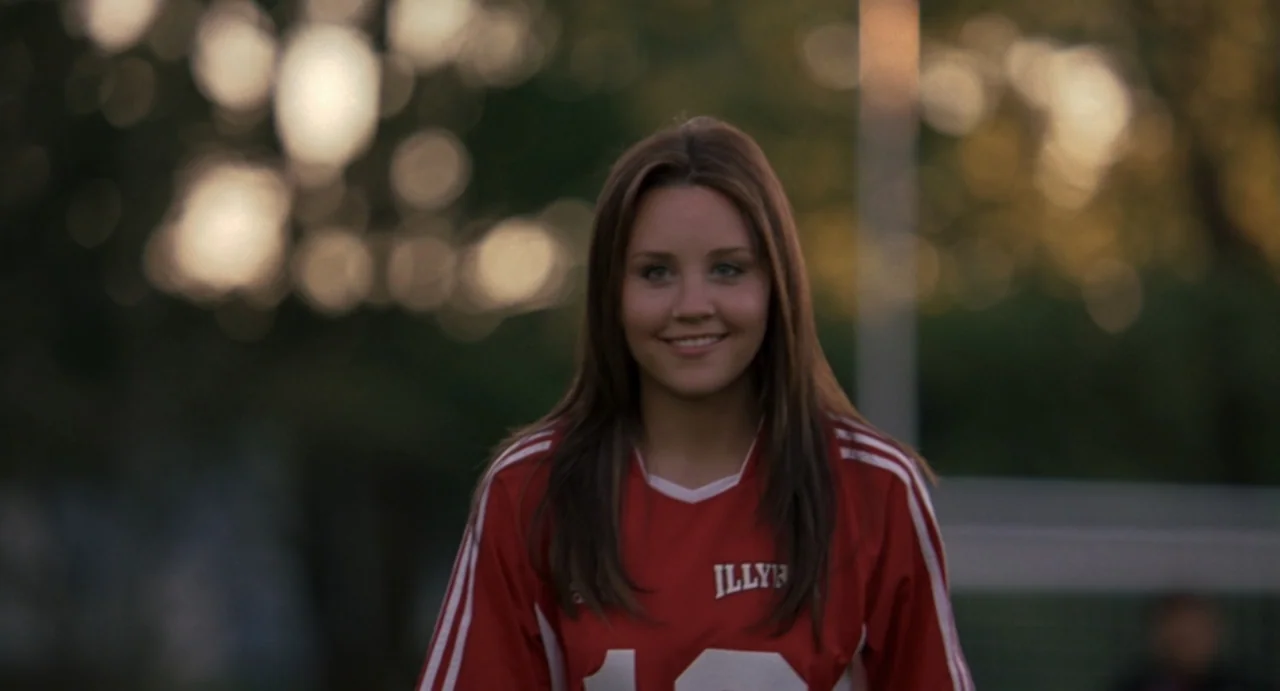 She's the Man (2006) movie still: medium — A sports field at golden hour features blurred trees in the background bokeh. A young woman in a red…