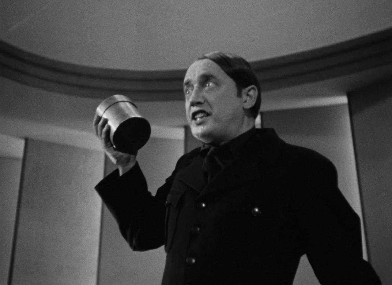 Krakatit (1948) movie still: medium — A man stands in a minimalist room with curved architectural walls. He holds a small cylindrical tin canister…