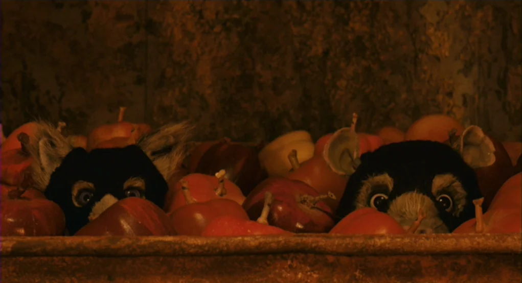 Fantastic Mr. Fox (2009) movie still: closeup — A pile of red apples sits in a shallow wooden crate inside a dark room. Two small puppet figures…
