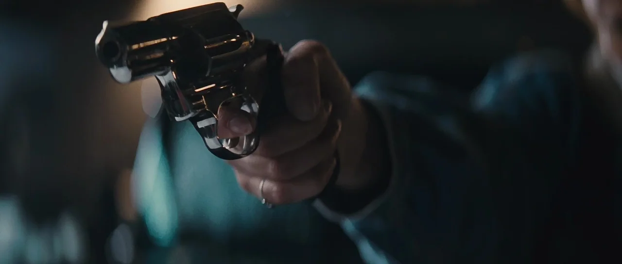 Thelma & Louise (1991) movie still: closeup — A dark, indistinct indoor space with minimal ambient light. A hand holds a polished revolver aimed…