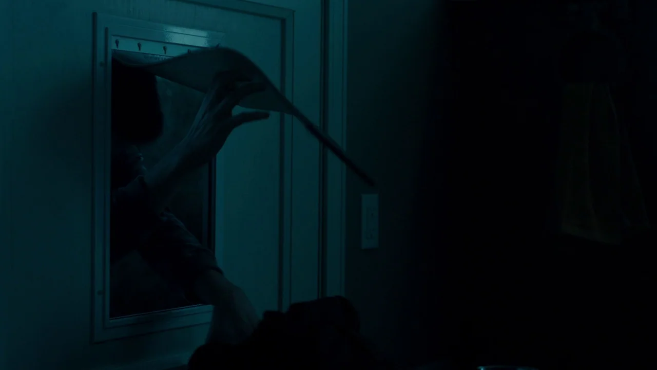 Fright Night (2011) movie still: medium — A dark, shadowed mudroom wall features a square pet door with a white frame. An unidentified hand reaches…