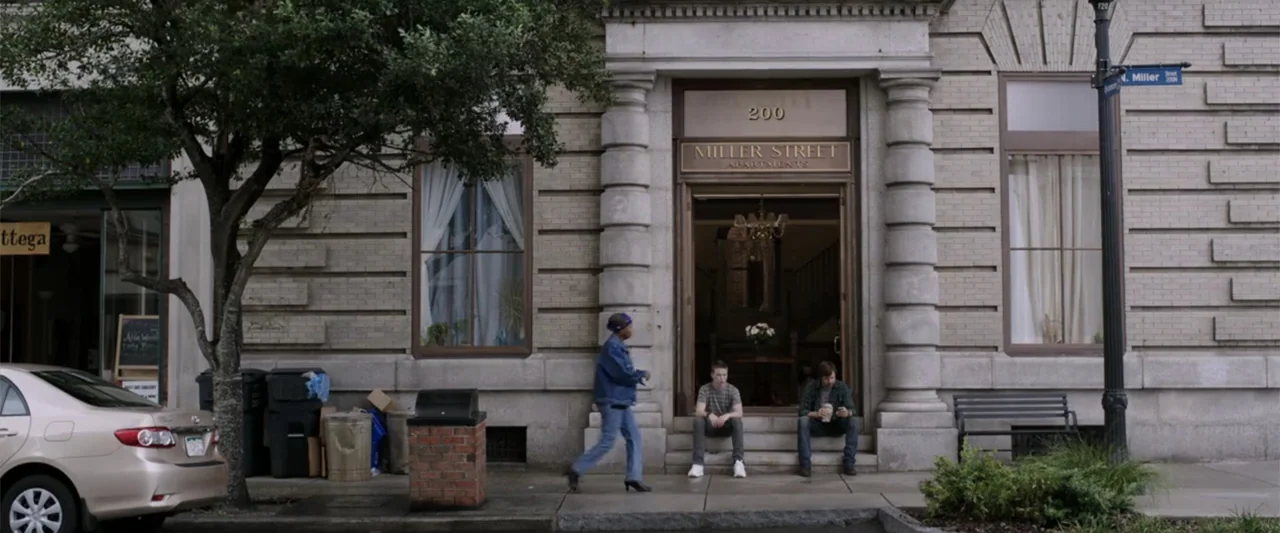 We're the Millers (2013) movie still: wide — A stone apartment building facade with a large central entryway and brick masonry. Three people stand…