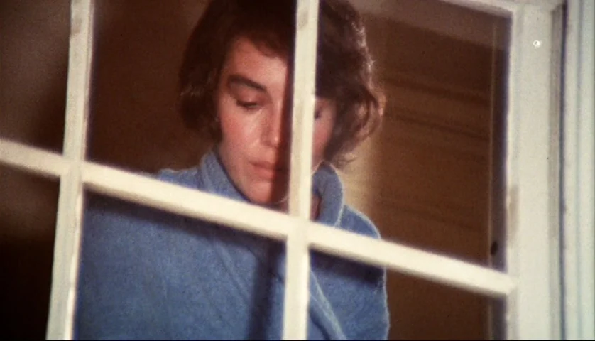 Let’s Scare Jessica To Death (1971) movie still: closeup — A woman stands behind a multi-pane glass window inside a room. She peers through the…