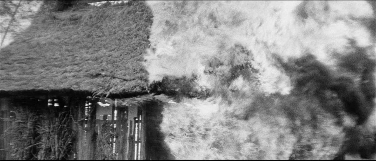 Kuroneko (1968) movie still: wide — A traditional thatched roof building stands partially obscured by a massive, turbulent smoke cloud. The…