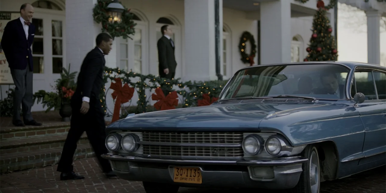 Green Book (2018) movie still: wide — A white colonnaded building entrance decorated for Christmas with festive wreaths and lights. A blue vintage…