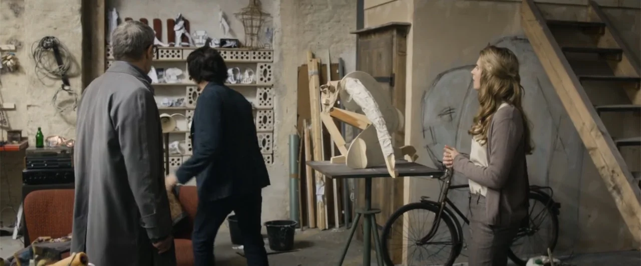 Heartburn (1986) movie still: medium — A cluttered workshop with rough plaster walls contains wooden armatures and sculptural materials. Two men and…