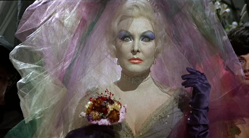 Juliet of the Spirits (1965) movie still: closeup — A woman dressed for a wedding stands behind a layered, semi-transparent purple veil. She holds a…