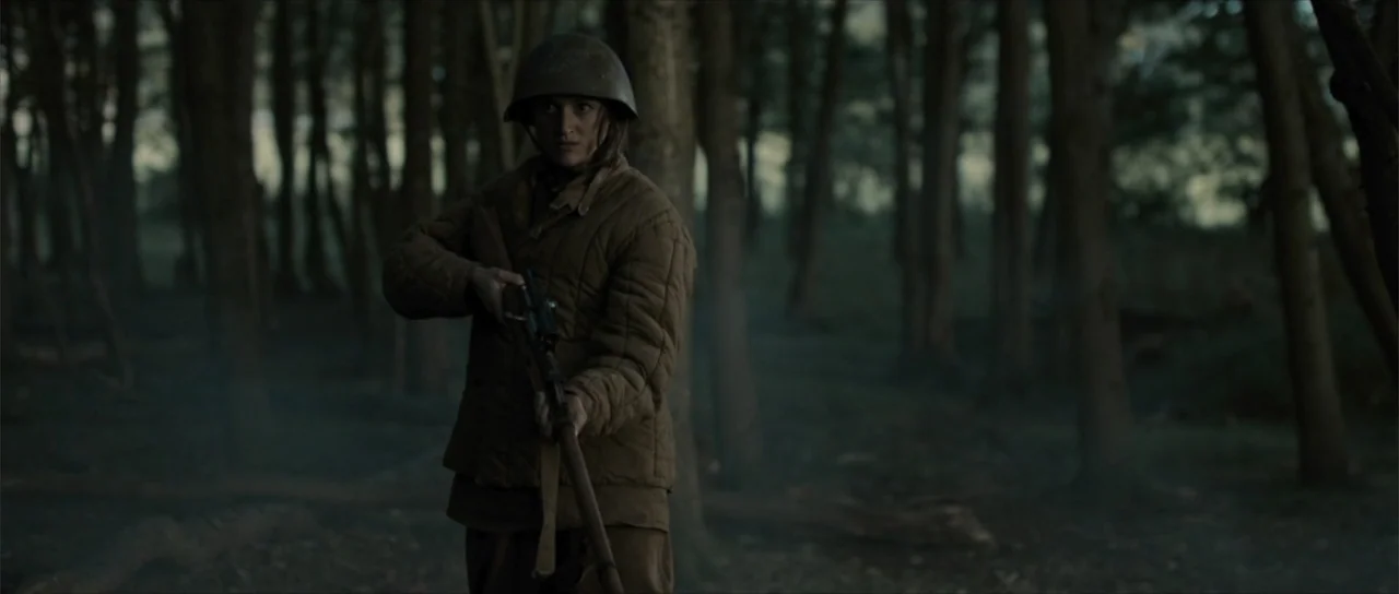 Sin retorno (2009) movie still: medium — A dense woodland with tall thin trees and a hazy, dim atmosphere. A soldier in 1940s field gear stands in…