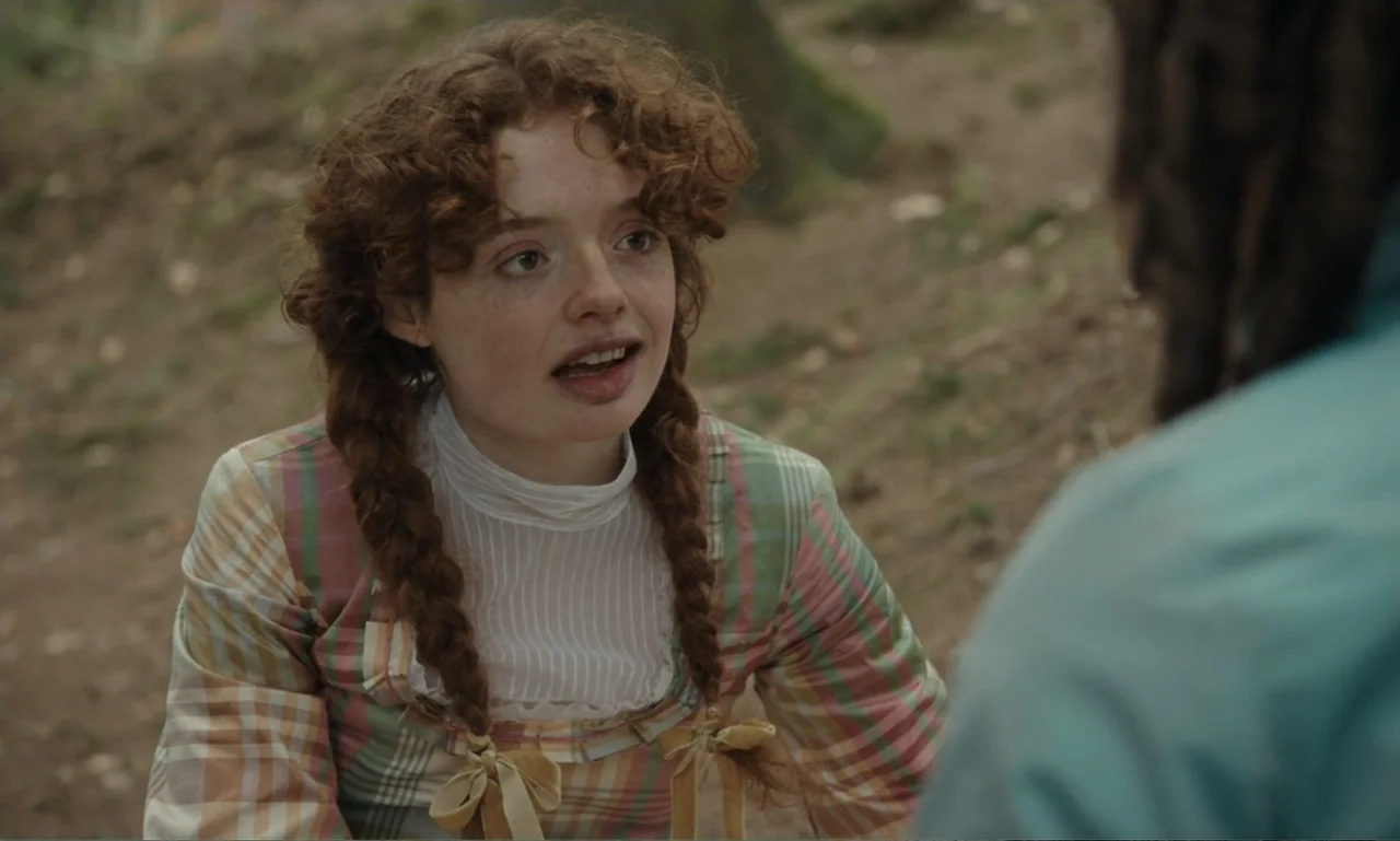 The Ugly Stepsister (2025) movie still: medium — A wooded area with soft, out-of-focus foliage in the background. A young woman with braided auburn…