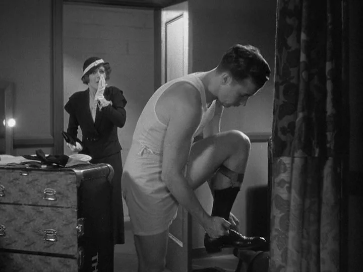 42nd Street (1933) movie still: fullbody — A dimly lit room contains a large vintage trunk and draped fabric curtains. A man in athletic gear laces…