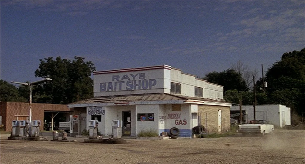 Sex, Lies And Videotape movie still: establishing — A worn bait shop stands at a rural gas station with dirt grounds. A white convertible pulls away…