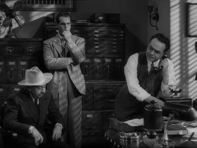 Double Indemnity (1944) movie still: medium — An office filled with wooden filing cabinets features a desk, a fan, and documents. Three men gather;…