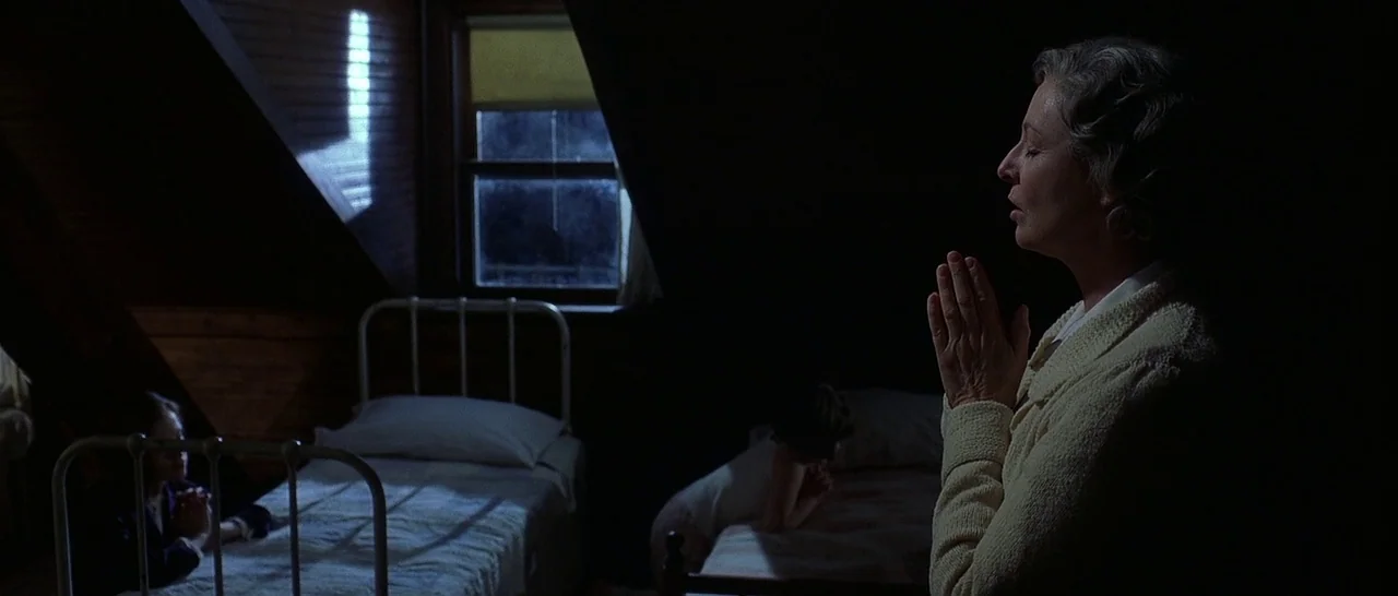 The Cider House Rules movie still: medium — An attic room features two white iron beds placed near a dark window frame. A woman stands in the…