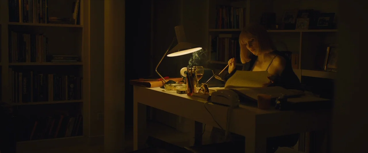 A Most Violent Year (2014) movie still: medium — A dimly lit home office with bookshelves filled with books flanking the desk. A woman sits at a…