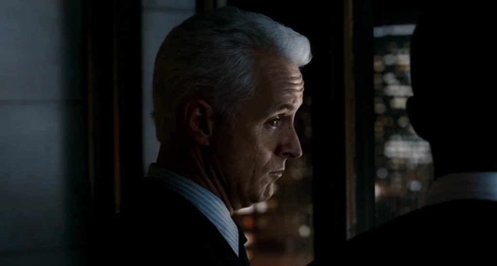 The Adjustment Bureau (2013) movie still: closeup — An interior space at night overlooks a distant city skyline through a dark window. A man with…