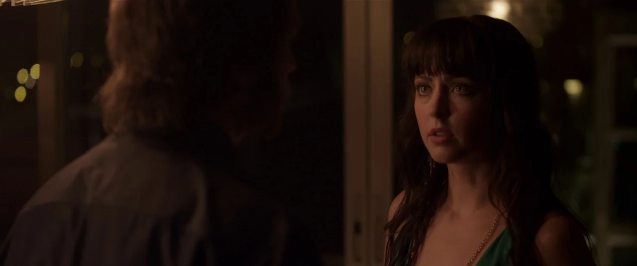 American Mary (2012) movie still: medium — An interior living room with dark walls at night featuring bokeh light reflections. A woman faces an…