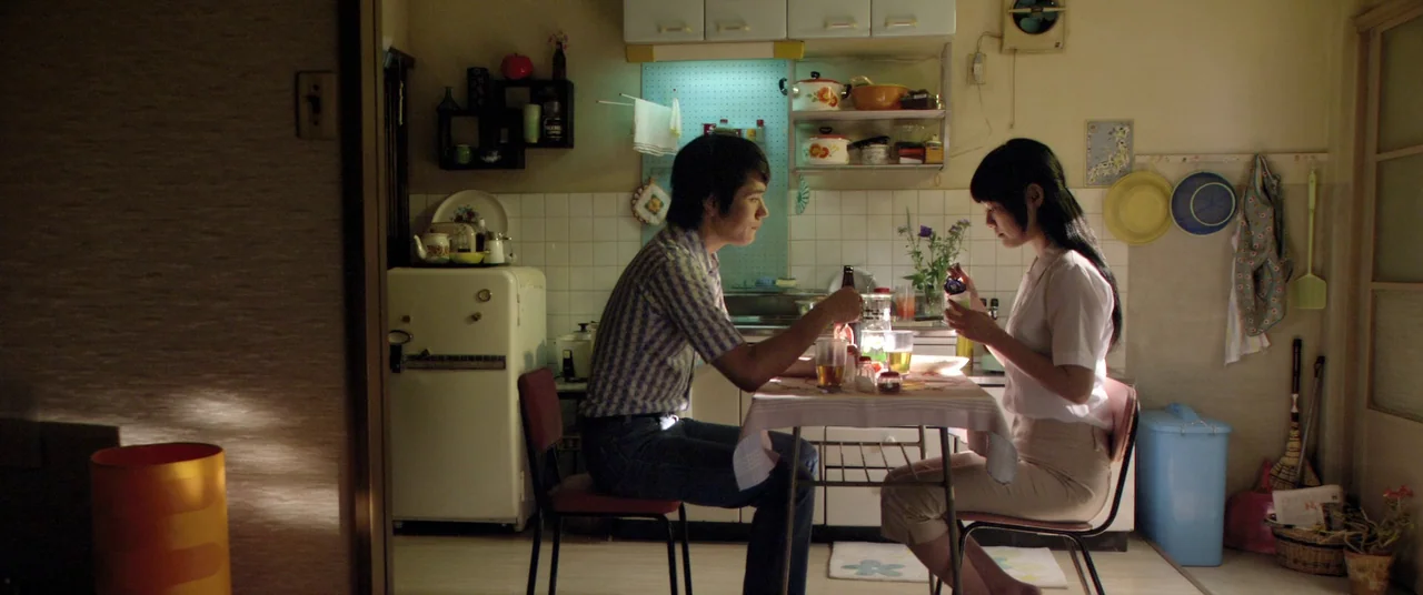 Norwegian Wood (2010) movie still: wide — A modest apartment kitchen features tiled walls, open shelving, and a small dining table. A young man and…