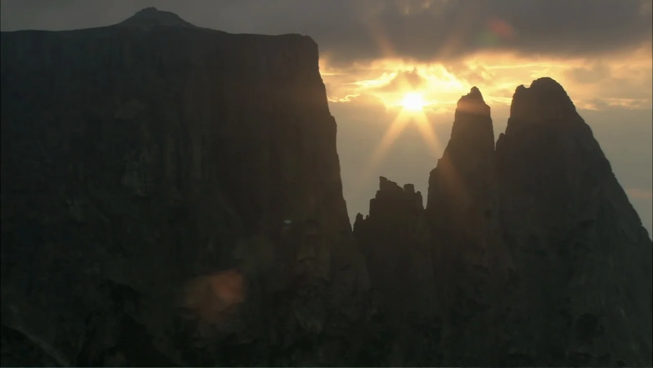 The Alps from Above: Symphony of Summits (2014) movie still: establishing — Jagged rocky mountain peaks stand against a bright sunset sky with…