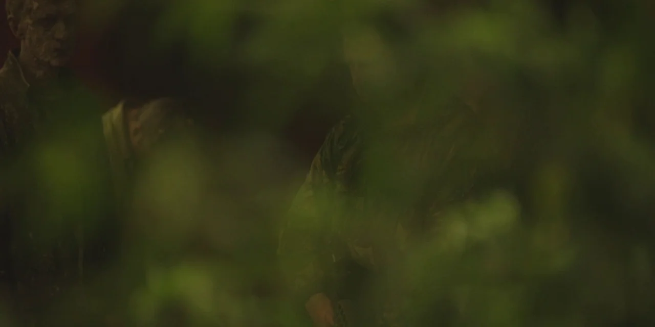 The Girl With All The Gifts (2016) movie still: medium — A dense forest environment features heavy foliage obscuring the view of the subjects. Two…