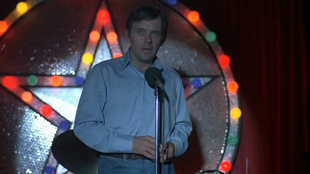 Magic (1978) movie still: medium — A dimly lit cabaret space features a large star-shaped neon sign with multicolored bulbs. A man in a blue…