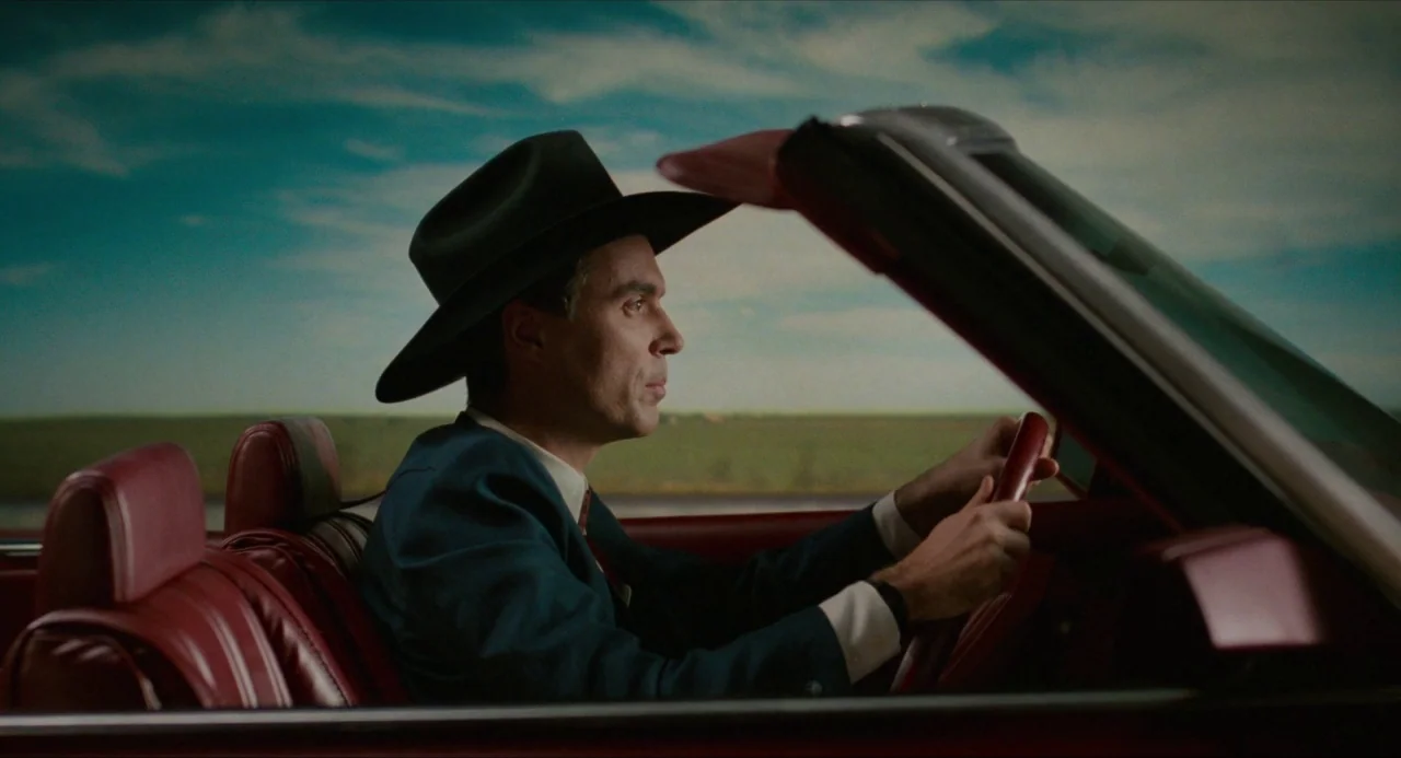 True Stories (1986) movie still: medium — A man drives a red convertible in front of a painted landscape backdrop. The artificial sky and horizon…