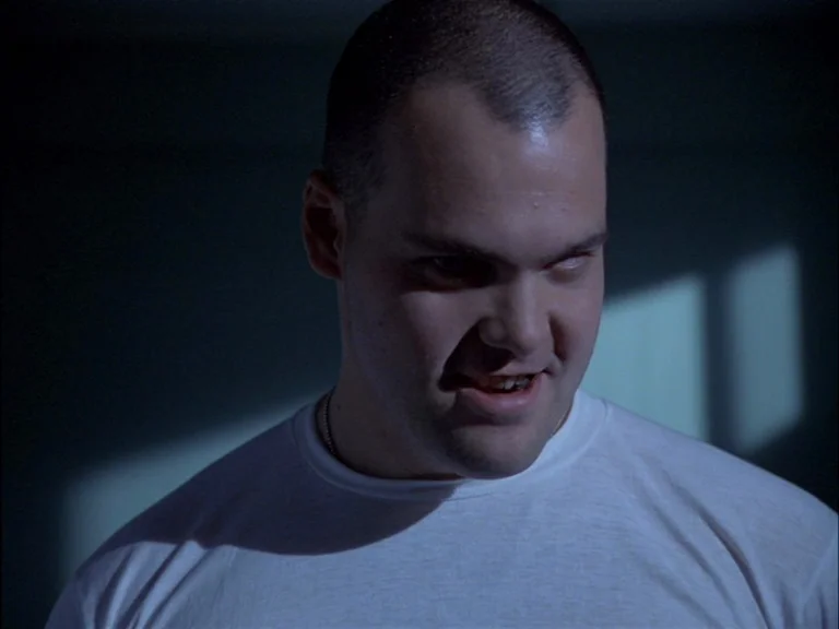 Full Metal Jacket (1987) movie still: closeup — A dimly lit room provides the backdrop for a close-up of a soldier. The man stares intensely into…