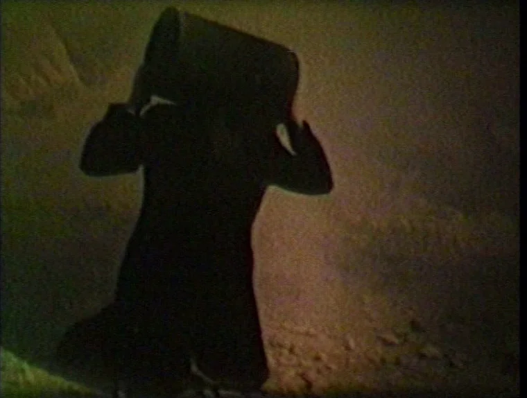 The Angelic Conversation (1985) movie still: fullbody — A dark outdoor space with uneven, rocky terrain visible at the bottom of frame. A human…