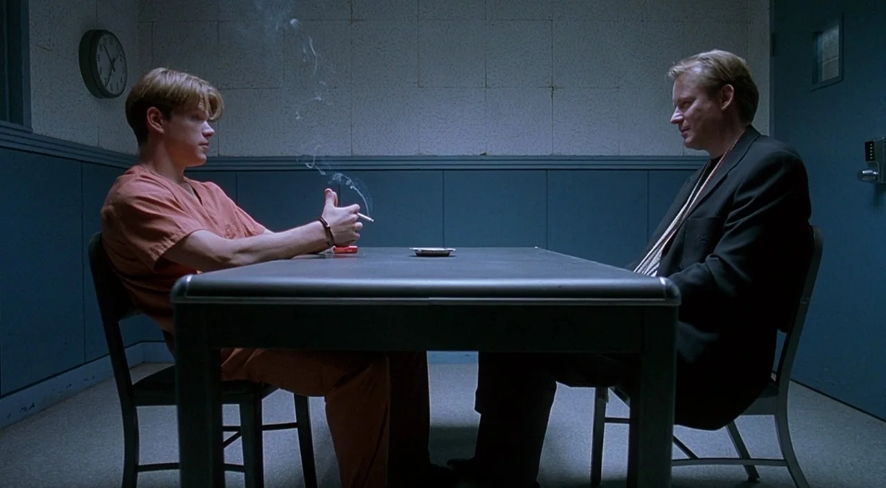 Good Will Hunting (1997) movie still: wide — A spartan interrogation room with light blue walls features a single metal table. A young man in an…