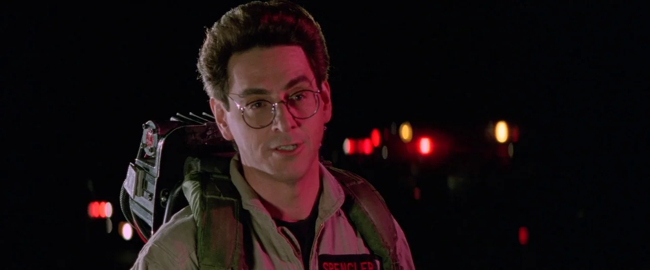 Ghostbusters 2 (1989) movie still: closeup — A dark night setting with red emergency lights blurring in the deep background. A man in a jumpsuit…