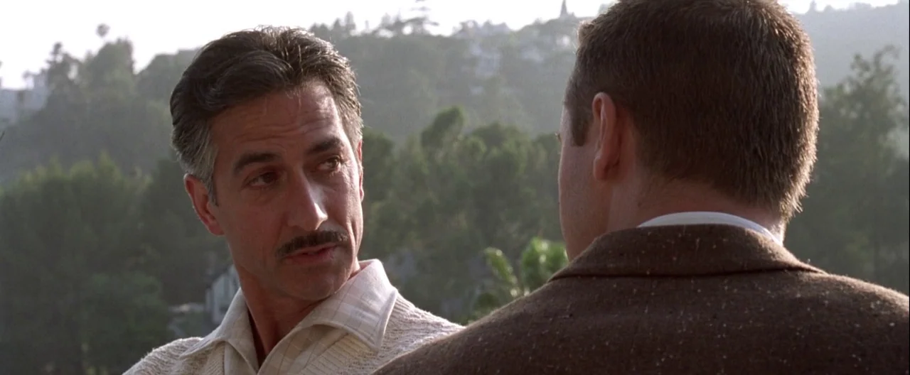 L.A. Confidential (1997) movie still: medium — A man looks at his companion on a balcony with a hillside background. The two men have a conversation…