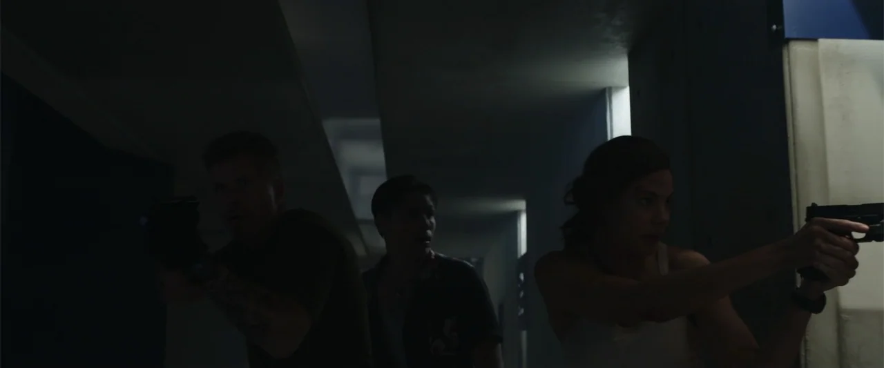 Black Site (2022) movie still: medium — A dark, industrial corridor features sharp geometric lines and recessed wall panels. Three armed individuals…