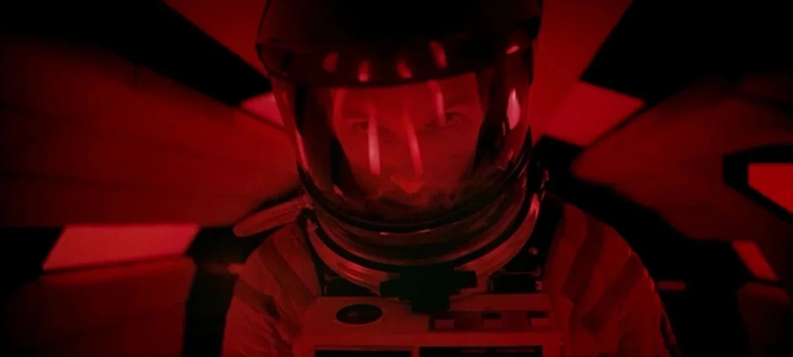 2001: A Space Odyssey (1968) movie still: closeup — A dimly lit interior of a futuristic spacecraft cabin filled with deep red light. An astronaut…