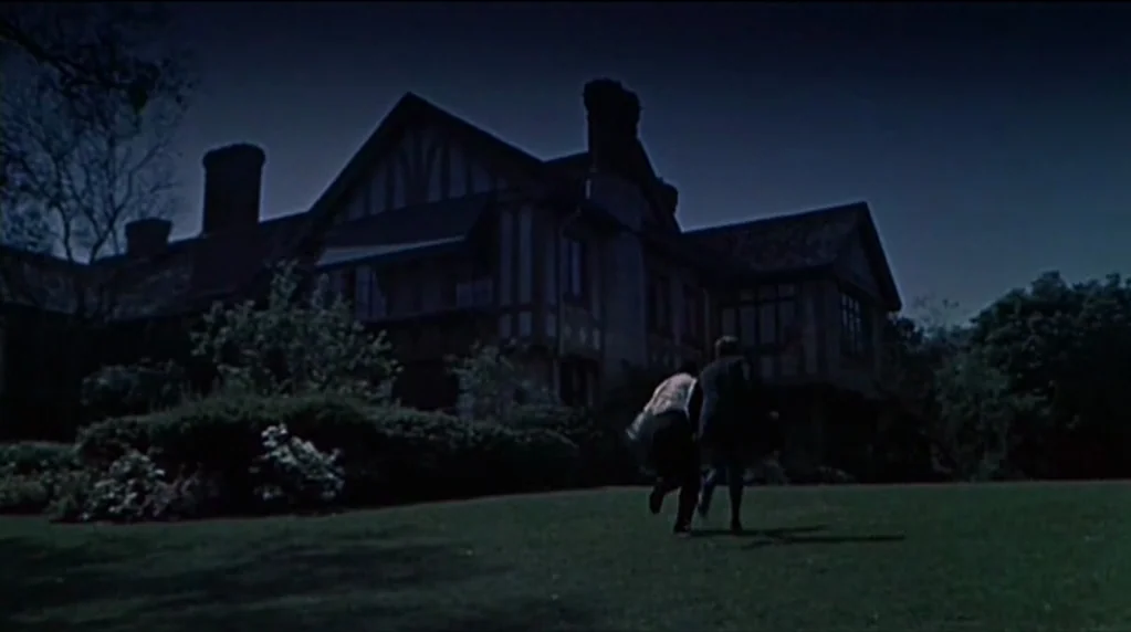 Artists and Models (1955) movie still: wide — A large Tudor-style mansion looms over a dark manicured lawn at night. Two men run across the grass…