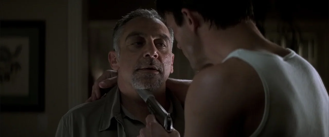 Enough (2002) movie still: medium — A dimly lit room provides the backdrop for a confrontation between two men. One man holds a metallic handgun…