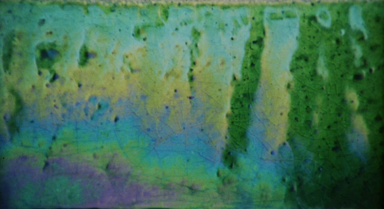Secret Ceremony (1968) movie still: closeup — A close-up view of a cracked, glazed ceramic surface. The glaze features layered pigments of green,…