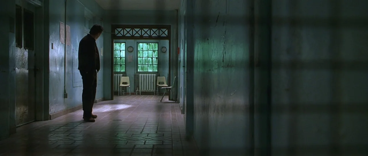 Don't Say a Word (2001) movie still: fullbody — A dimly lit hospital corridor features teal-colored walls and a tile floor. A man stands alone in…
