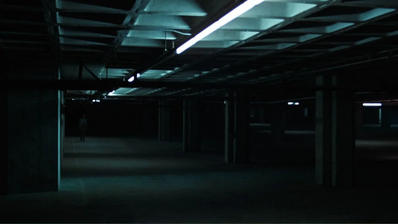 All the President's Men (1976) movie still: wide — A dark, cavernous concrete parking garage features structural pillars and overhead fluorescent…