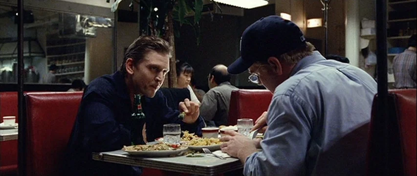 25th Hour (2002) movie still: medium — A diner booth with red vinyl seating and a metallic table under bright lights. Two men sit opposite each…