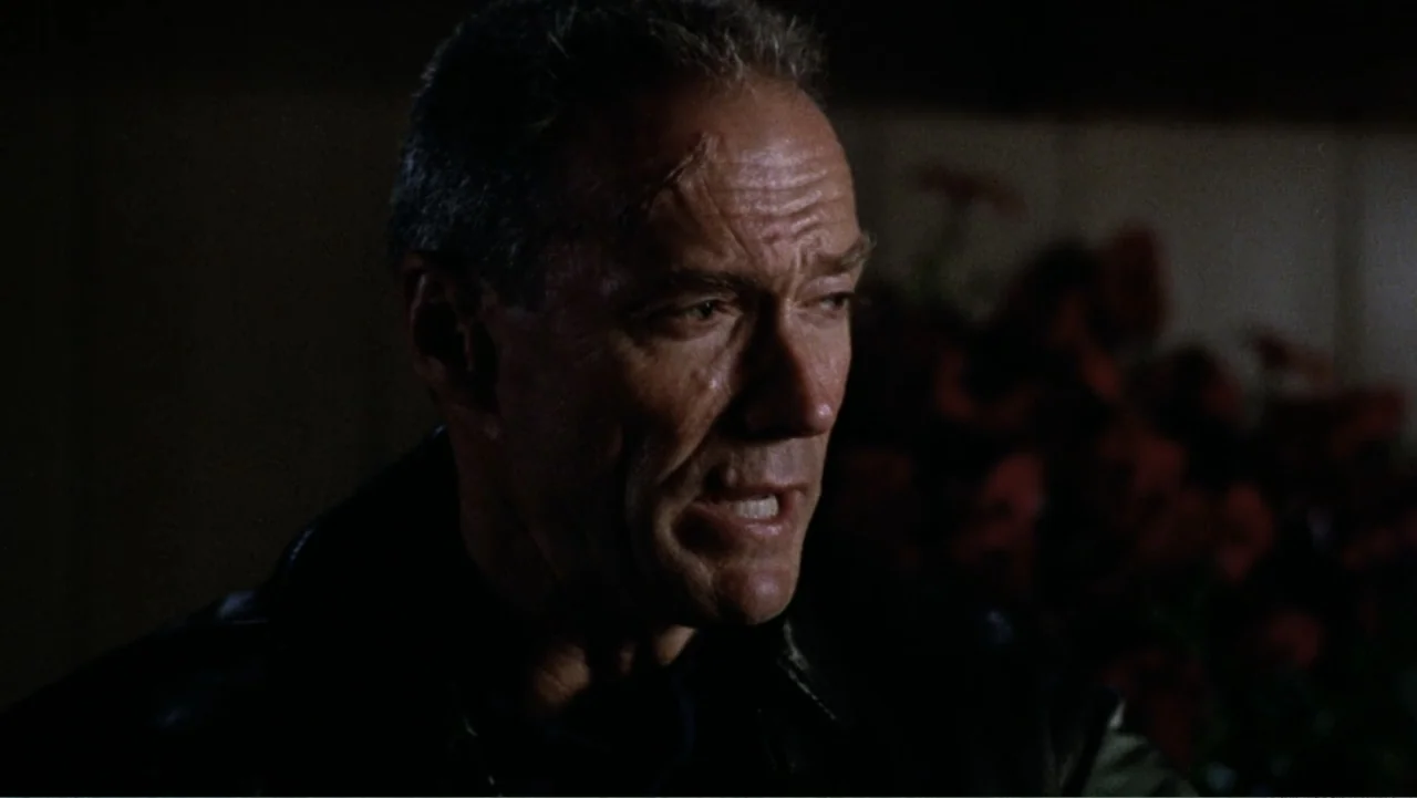 Heartbreak Ridge (1986) movie still: closeup — A dimly lit interior room features a man standing before a dark background. He wears a leather jacket…