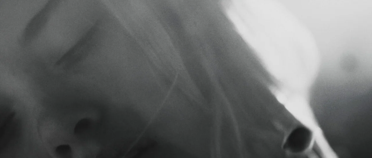Starfish (2018) movie still: closeup — A close-up view of a face resting against a soft surface in shadow. Long hair strands drape over the cheek…
