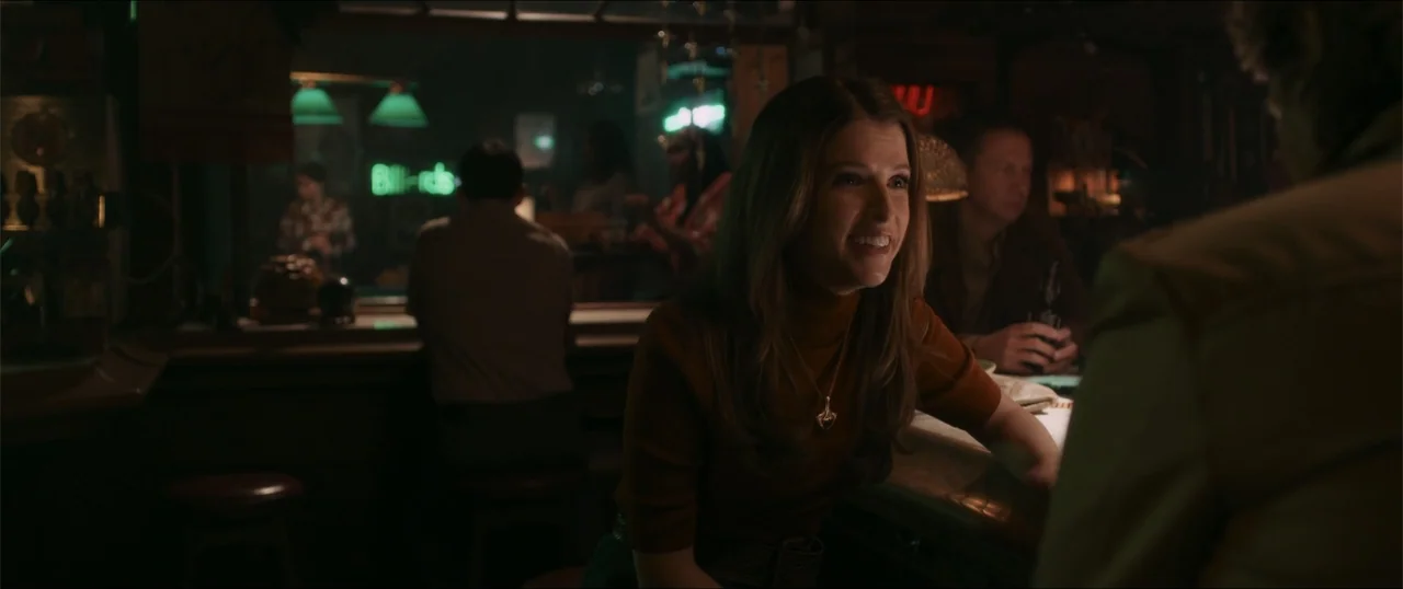 Woman of the Hour (2024) movie still: medium — A dimly lit 1970s bar with a wooden counter and green neon signage.