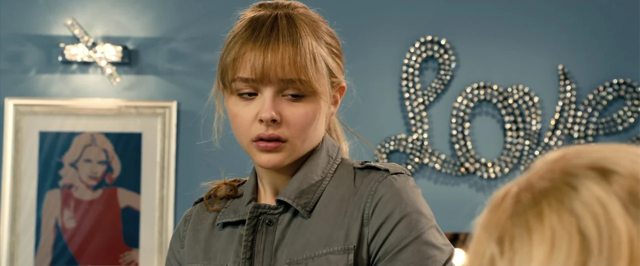 Kick-Ass 2 (2013) movie still: medium — A blue-walled bedroom interior decorated with a beaded word wall art piece. A young woman with blonde hair…
