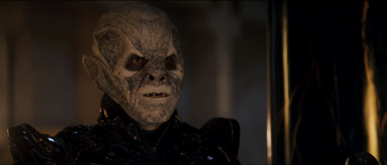 Star Trek: Nemesis (2002) movie still: closeup — An alien character with wrinkled grey skin is situated inside a dim futuristic command center. The…