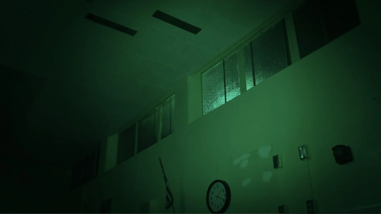 The Gallows (2015) movie still: establishing — A dark school hallway is visible under the intense monochromatic glow of night vision. An analog wall…