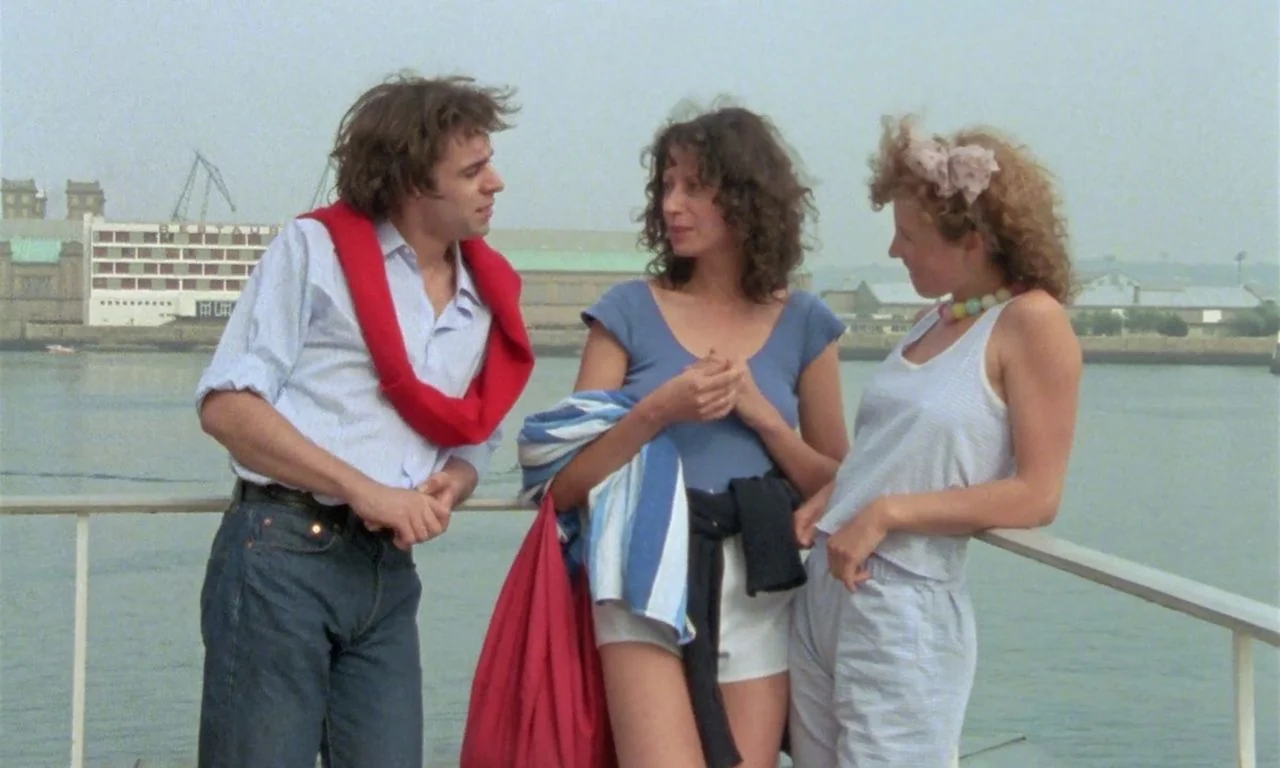 The Green Ray (1986) movie still: medium — A group of three people stand at the metal railing of a ferry deck. In the background a large industrial…