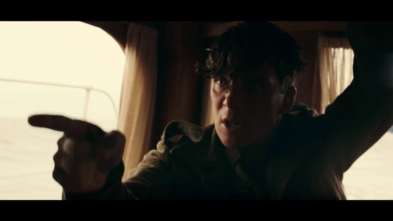 Dunkirk (2017) movie still: medium — A dimly lit boat cabin features wooden paneling and curtains over an oval window. A man directs a sharp gesture…